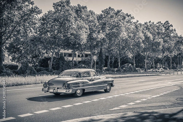 Fototapeta Czarno-białe monochromatyczne zdjęcie amerykańskiego samochodu oldtimer z lat 50. Vintage samochód USA na ulicy w słoneczny letni dzień. Retro podróży, koncepcja ruchu.