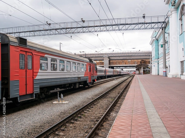 Fototapeta The passenger train at the railway station on a cloudy day. Electric train, wagons, railway platform.