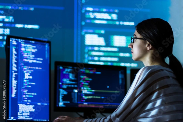 Fototapeta Software developer freelancer woman female in glasses work with program code C++ Java Javascript on wide displays at night Develops new web desktop mobile application or framework Projector background