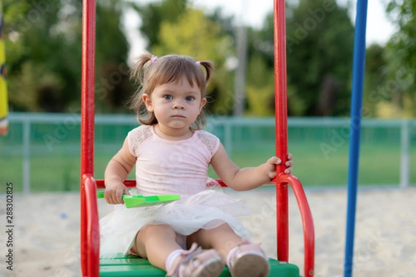 Obraz Funny little child, adorable preschooler girl in pretty dress having fun on a swing in the park on summer day