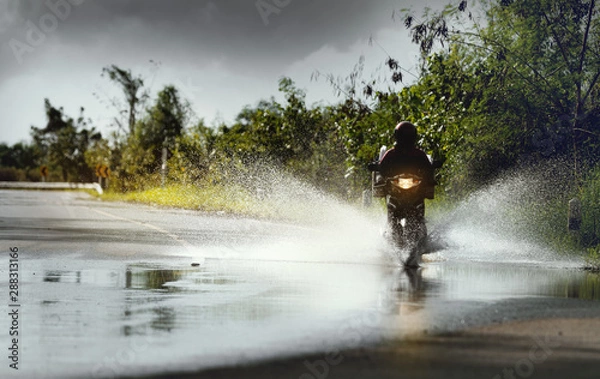 Fototapeta Motorcycle run through flood water after hard rain with water spray from the wheels .Stop action ( capture with the high speed shutter) and selective focus.