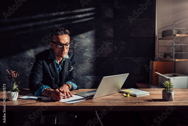Fototapeta Businessman writing notes and contemplating in his office