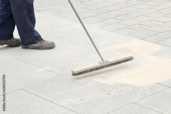 Fototapeta Pavement construction worker filling the block joints with sand using long broom