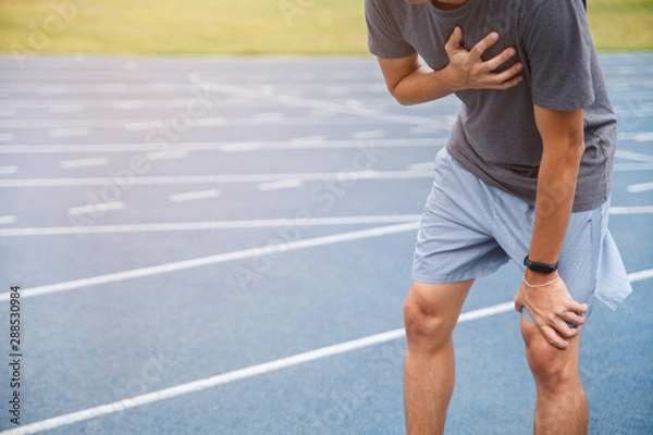 Obraz Man runner athlete chest injury and pain. Man suffering from painful chest or Symptoms of heart disease while running on the blue rubberized running track.