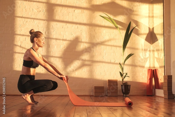 Fototapeta Woman preparing for doing yoga, lying down a mat on the floor