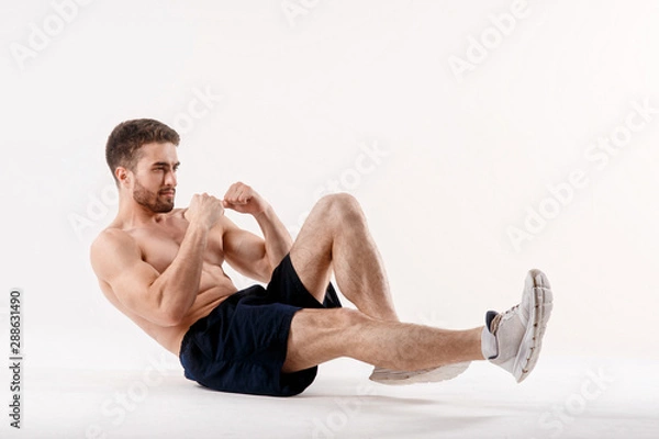 Fototapeta young man with a beard of a sports physique does an exercise on the muscles of the abdominal cavity on a white isolated background, the athlete goes in for sports, exercise on the muscles of the press
