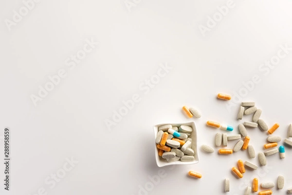 Fototapeta Bowl with scattered pills on white background. Flat lay.