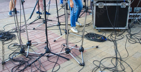 Fototapeta Close up view of tangled black wires and cables plugged and microphone stand on the ground, chaos after concert