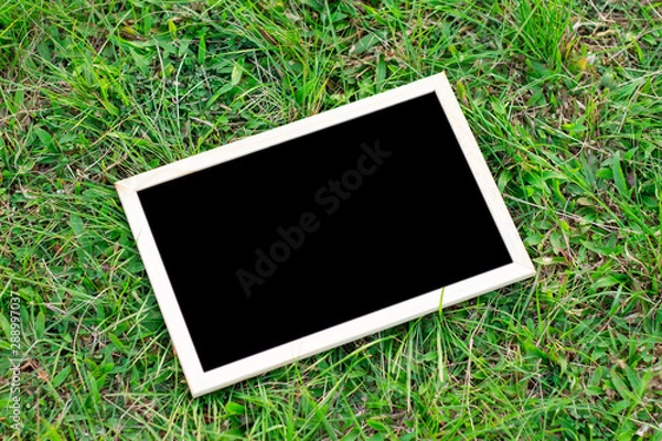 Fototapeta Mock up image of a blackboard put on the green grass field floor background.