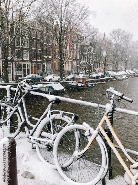 Fototapeta Snowy bicycles on the bridge in the city center Amsterdam Netherlands. Blizzard on winter in the Netherlands. Bicycles covered with snow on a bridge. Snowfall in capital Netherlands