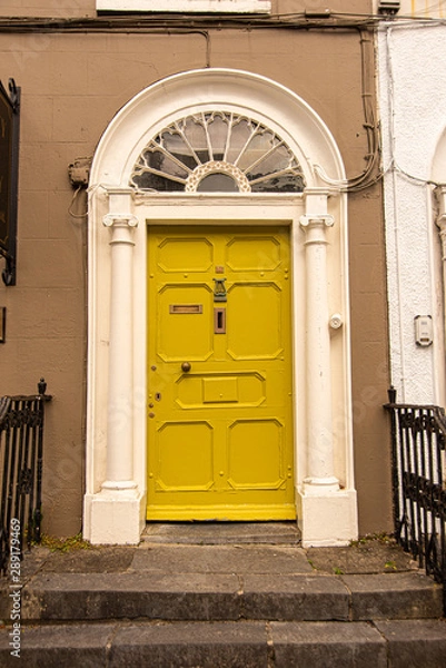 Fototapeta A yellow door with columns in a street of row homes in Ireland