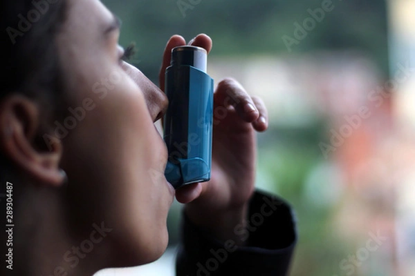 Obraz Health and medicine - Young girl using blue asthma inhaler to prevent an asthma attack.