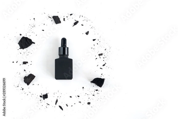 Fototapeta Black serum bottle surrounded by charcoal on white background with copy space, Mockup product