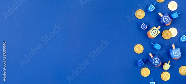Fototapeta Dark blue background with multicolor dreidels and chocolate coins. Hanukkah and judaic holiday concept. Horizontal, banner format style