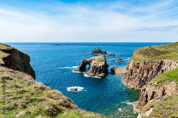 Fototapeta Dry grassy cliffs overlooking Enys Dodnan Arch on a partially sunny day in Land’s End, UK.