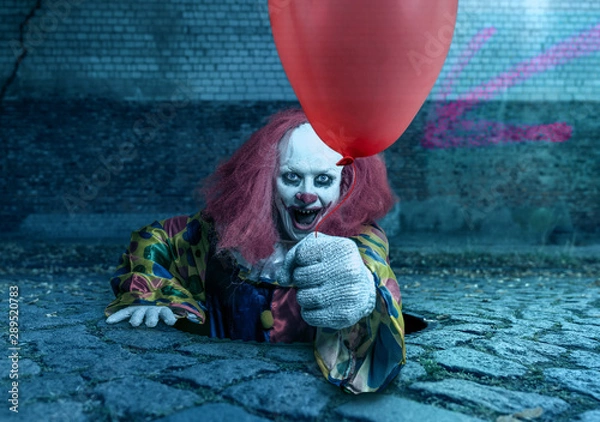 Fototapeta scary clown with a balloon rising from the sewer