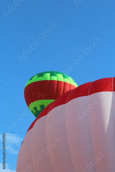 Fototapeta Ballons Festival - Balloon Festival, exhibition of hot-air balloons in the city park. Hot air balloons in preparation for the flight and in the background hot air balloon hovering in flight