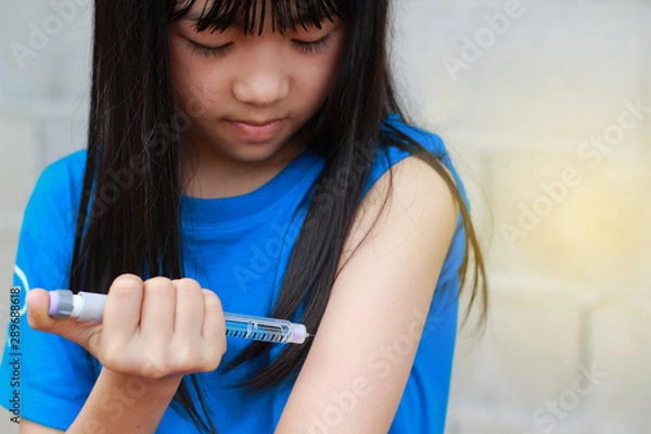 Obraz An Asian children girl using insulin pen.Self insulin injection.