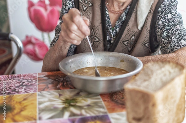 Fototapeta The old woman eats soup, charity food for the poor pensioners, social reform