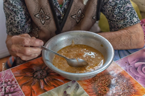 Fototapeta The old woman eats soup, charity food for the poor pensioners, social reform