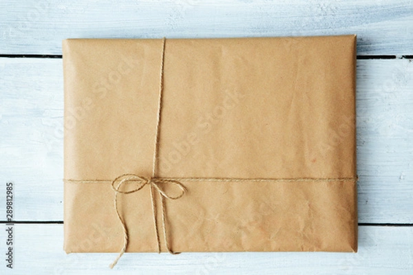 Fototapeta Close up Christmas style rustic brown paper package tied up with strings. White wood floor background.