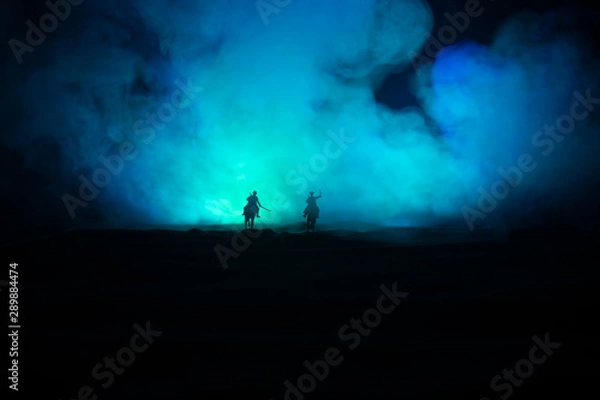 Fototapeta World war officer (or warrior) rider on horse with a sword ready to fight and soldiers on a dark foggy toned background. Battle scene battlefield of fighting soldiers.