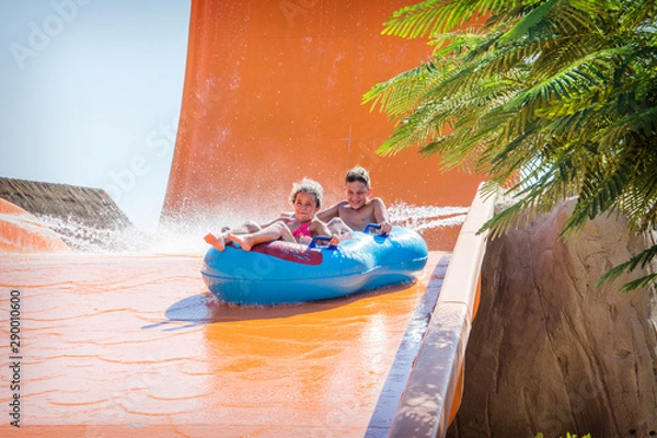 Fototapeta In the summer, on a bright sunny day, in a water park, a brother and sister ride off a slide on an air mattress.