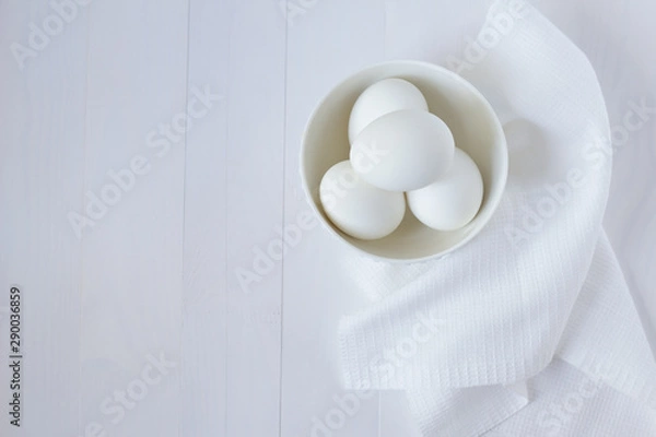 Fototapeta White eggs in a plate on a towel stand on a white wooden table with place for text