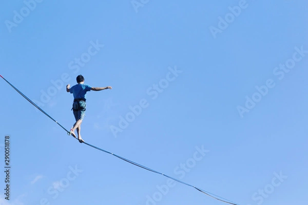 Obraz A man is walking along a stretched sling. Highline in the mountains. Man catches balance. Performance of a tightrope walker in nature. Highliner on the background of the mountains.
