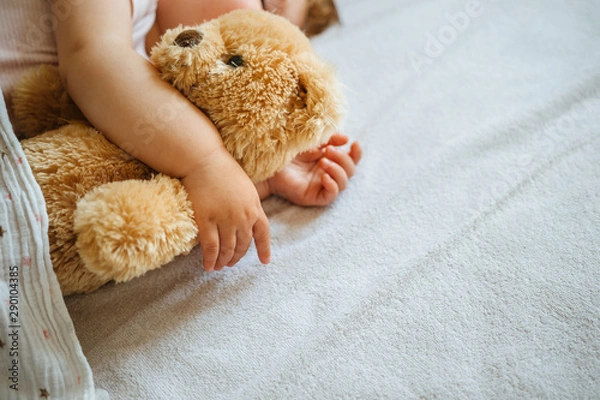 Fototapeta Little baby sleeping and embracing soft toy bear, close-up on hands