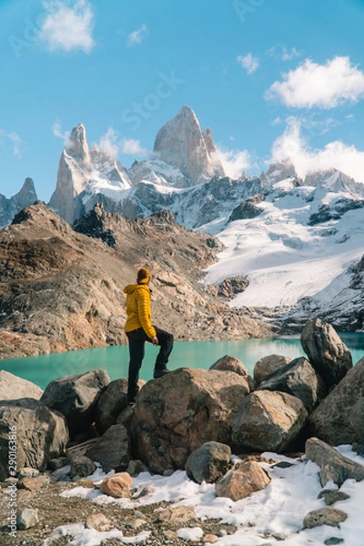 Fototapeta Tourist man at Mount Fitzroy, Patagonia trek. Scenic view of snowcapped mountain tops. Blue sky, turquoise blue lake and scenic rock landscape. Shot in Argentina. Nature, travel, adventure, hiking.