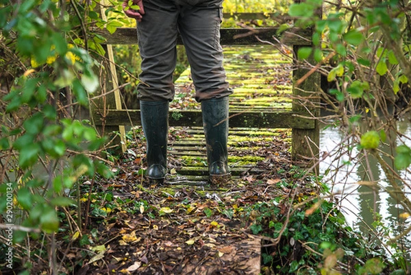 Fototapeta Men in rubber boots on the rustic wooden bridge in the forest