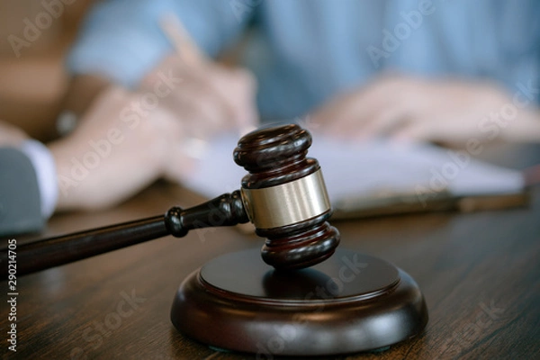 Obraz Judge gavel on wooden teable background with  businessman and female lawyers having a meeting at a law firm. Concepts of law.