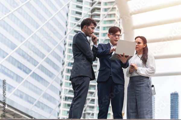 Fototapeta group of asian business people working and discussing something positive with his mature colleague and using a laptop at outdoor in the capital