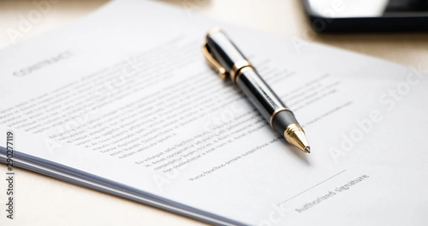 Fototapeta Close up of ball pen lying on a contract paper or application form on office desk, low angle view and selected focus. Signing the business contract concept.