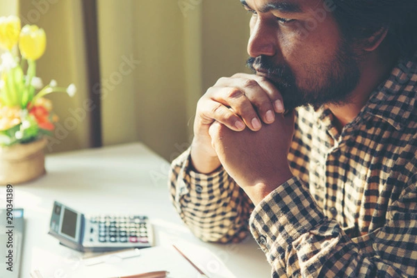 Fototapeta Serious businessman looking at laptop screen and thinking on problem while sitting in office.