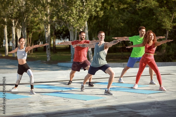 Fototapeta Group of young sporty people training together outdoors