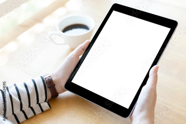 Fototapeta Hands holding black digital tablet pc with white blank screen on wooden table background in cafe.
