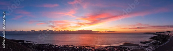 Fototapeta A panoramic of sun setting over the clouds and painting golden and pink colours across the skies. As the rocky shore and the white chalk cliffs of the Seven Sisters meets the sea in Eastbourne, UK.