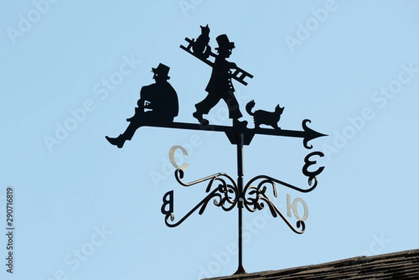 Fototapeta Weathervane in the form of people and cats.. A product made of metal on the roof of the house.