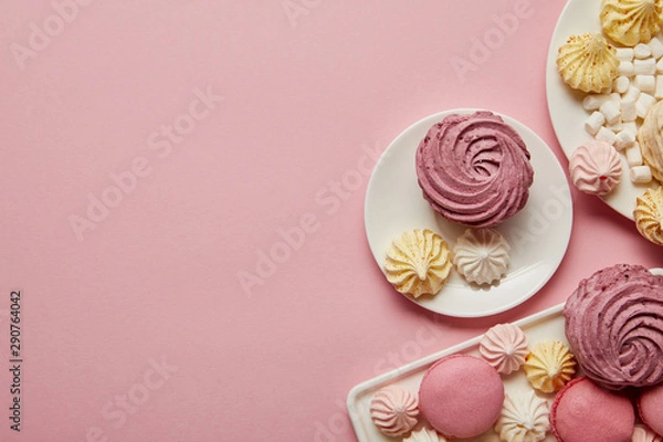 Fototapeta Top view of pink, white and yellow meringues, macaroons and marshmallows on pink background
