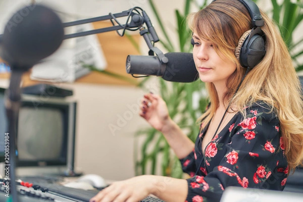 Fototapeta girl radio host with headphones speaks into a microphone on a radio station and reads a script