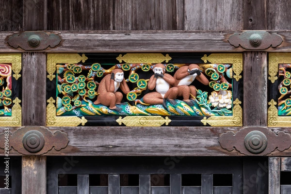 Fototapeta Symmetrical close up shot of a porcelain bas-relief portraing the three wise monkeys framed by a weathered wooden structure