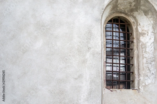 Fototapeta Medieval arched window with rusty grating on a light wall