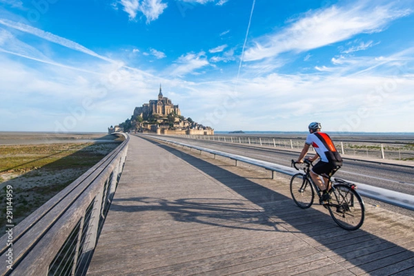 Fototapeta Cyclist driving on the only access road to Mont Saint Michael. The bicycle is one of the options allowed for access