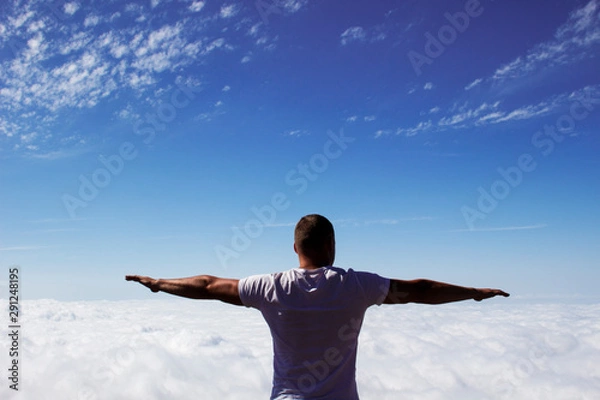 Fototapeta young man with open arms raised above the clouds