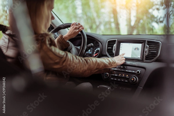 Fototapeta Woman girl in summer car interior in forest park, selects navigation touch screen, satellite internet application. Lost in search of a route, parking in the fresh air rest in the forest.