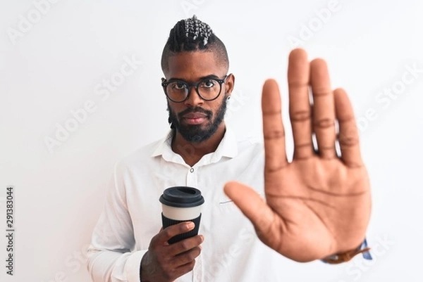 Fototapeta African american businessman with braids drinking coffee over isolated white background with open hand doing stop sign with serious and confident expression, defense gesture