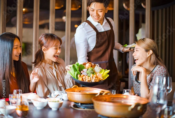 Obraz waiter  bring  vegetables for hot pot  and serving group of friends in restaurant