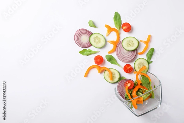 Obraz Glass bowl with fresh vegetables slices on white background, copy space